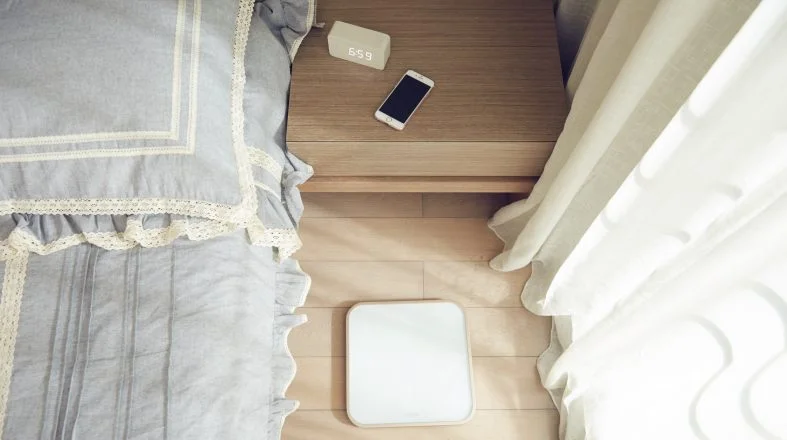 light blue bed on the left side of the photo and on the right side a night table with alarm and phone on it